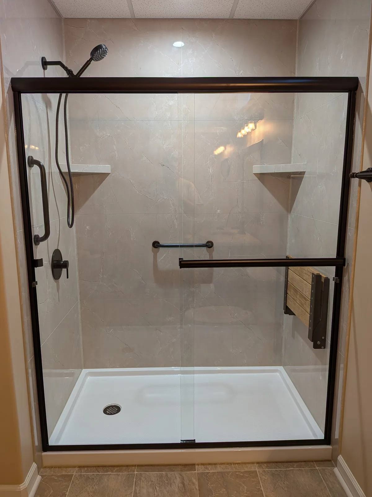 Head-on view of the bronze-framed walk-in shower, grab bars and fold-down seat