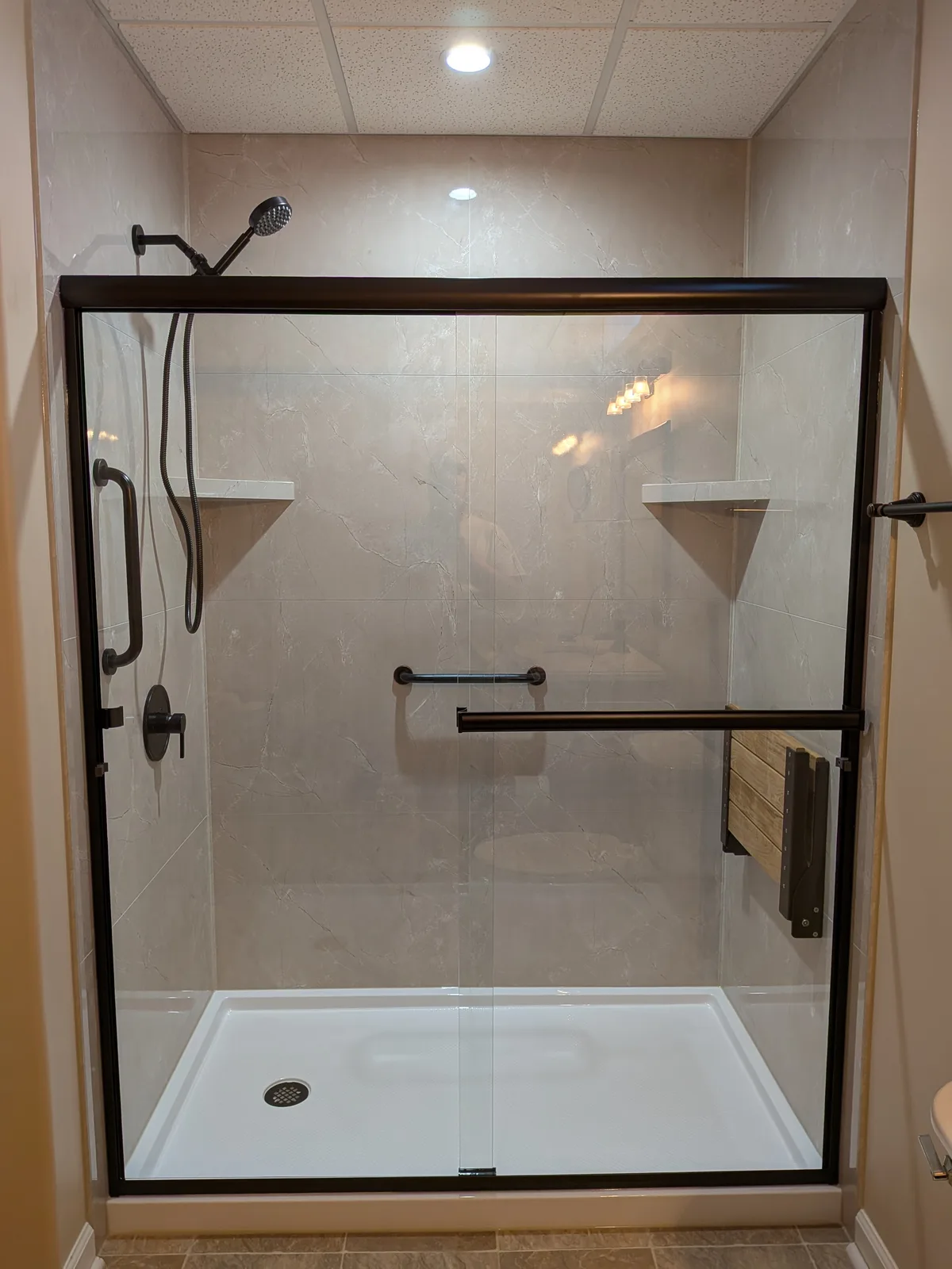 Bronze-framed shower doors and marble-look walls after the remodel
