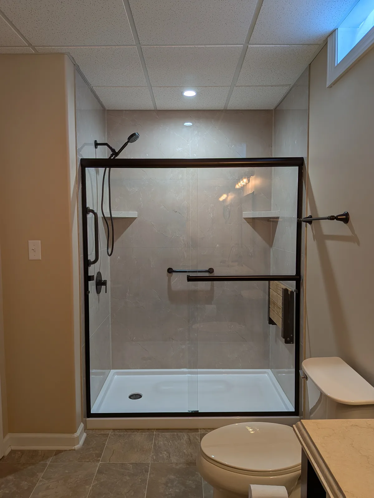 Walk-in shower with bronze-framed glass doors, marble-look walls and a low-threshold base